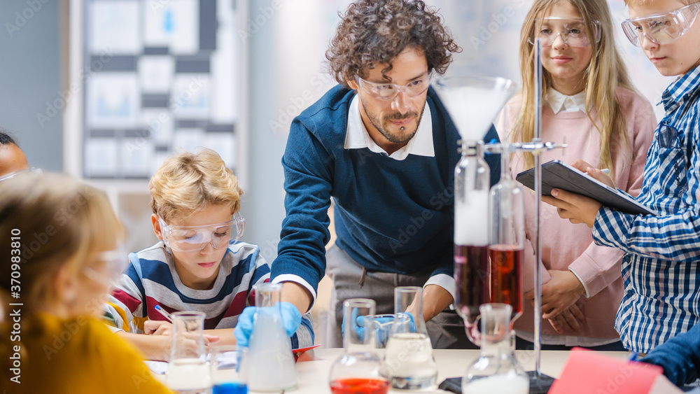 Elementary School Science Classroom: Enthusiastic Teacher Explains Chemistry to Diverse Group of Children, Shows them How to Mix Chemicals in Beakers. Children Use Digital Tablet Computers and Talk Elementary School Science Classroom: Enthusiastic Teacher Explains Chemistry to Diverse Group of Children, Shows them How to Mix Chemicals in Beakers. Children Use Digital Tablet Computers and Talk