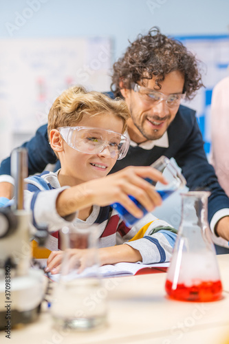 Elementary School Science Classroom: Little Boy Mixes Chemicals in Beakers, Enthusiastic Teacher Helps with Chemistry Science to a Child. Children Learn with Interest