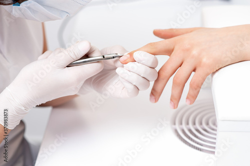 Close up of manicurist using manicure cutter to remove cuticle of female nails in manicure salon