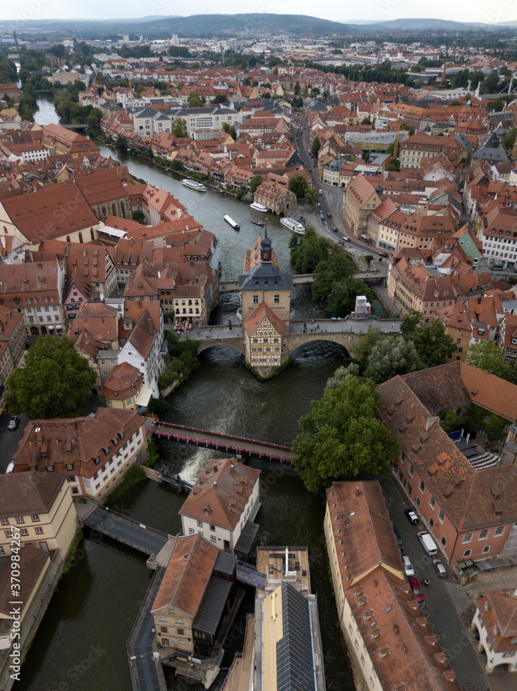 Aerial view of old town hall in Bamberg, Bavaria, Germany. House above river Main. Вridge, boats ancient historic half-timbered buildings with orange roofs. Beautiful cityscape.