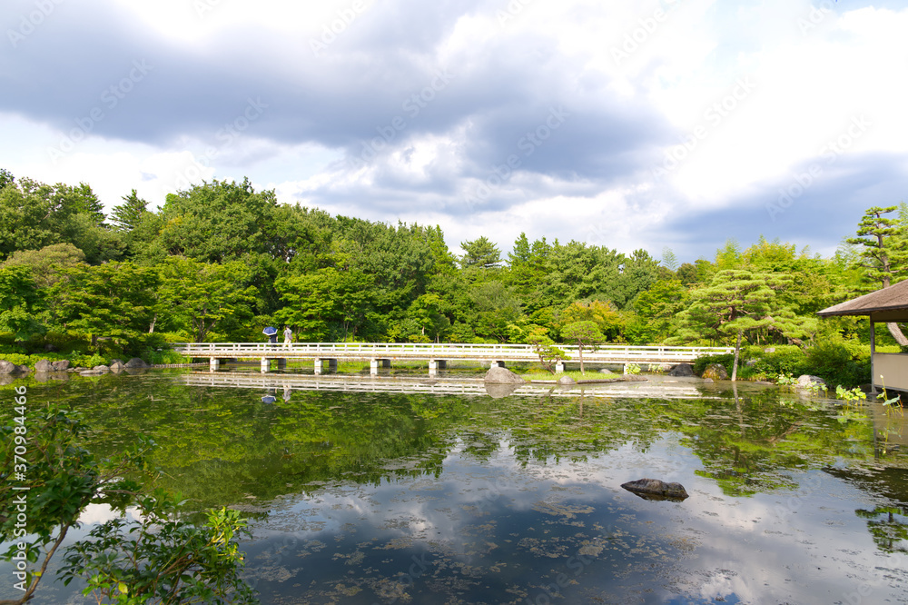 HDR natural Japanese style decoration park and garden, decorated greenery tree, vintage cement bridge, Japanese style house and bush with its mirror reflection on clear water pond.