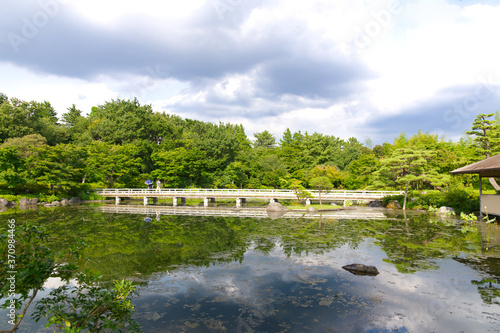 HDR natural Japanese style decoration park and garden  decorated greenery tree  vintage cement bridge  Japanese style house and bush with its mirror reflection on clear water pond.