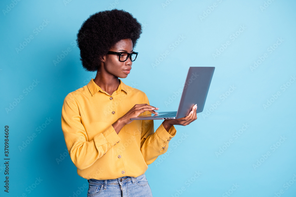 Photo of black skin big volume hairstyle serious calm woman hold laptop working managing remote online graphic design project wear specs jeans yellow shirt isolated blue color background