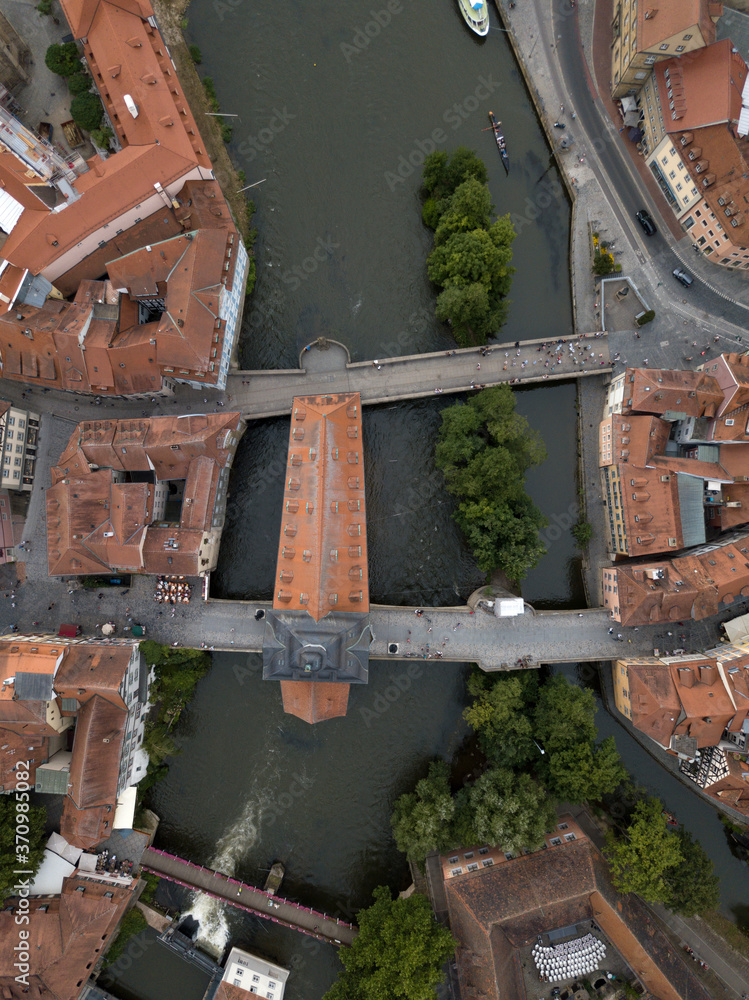 Aerial top down view of old town hall in Bamberg, Bavaria, Germany. House above river Main. Вridges, boats, trees, ancient historic half-timbered buildings with red orange roofs. Beautiful cityscape.