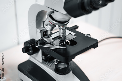 close-up of a microscope in a veterinary laboratory. medical research virus center in grayscale. eyepieces near, biomaterial under study with illumination at work.