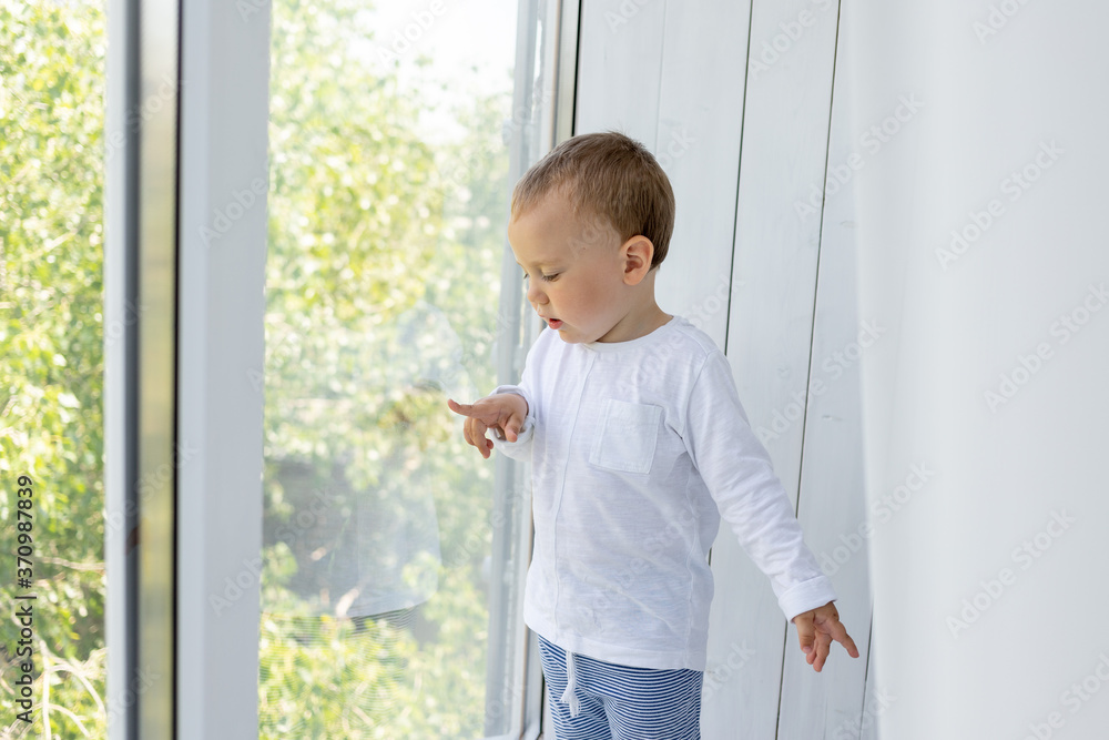 a small boy 2 years old is standing at the window and waiting for mom and dad a small boy 2 years old is standing at the window and waiting for mom and dad