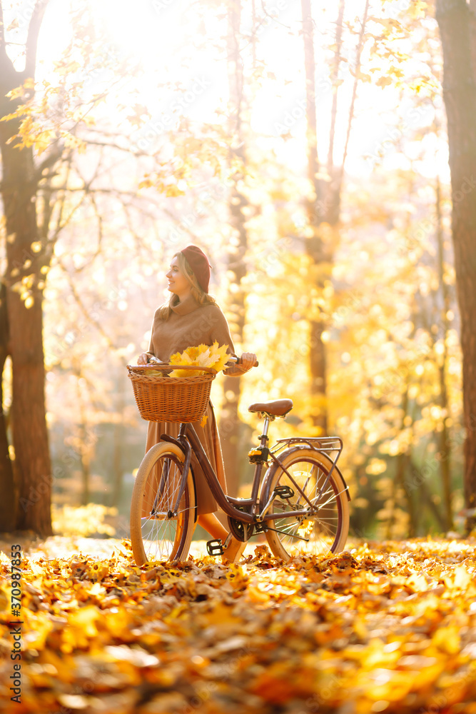 Stylish woman with a bicycle enjoying autumn weather in the park. Beautiful Woman walking  in the autumn forest. - obrazy, fototapety, plakaty 