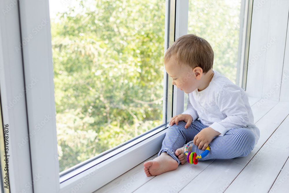 a small boy 2 years old is standing at the window and waiting for mom and dad a small boy 2 years old is standing at the window and waiting for mom and dad