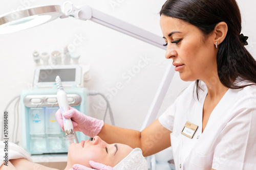 Beauty salon. The cosmetologist makes a water peeling for the client. Device for the procedure in the background.Professional skin care and beauty concept