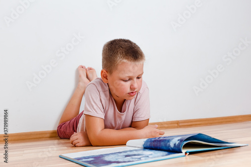 eight-year-old boy lies on the floor reading a big book