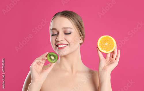 Young woman with cut kiwi and orange on pink background. Vitamin rich food