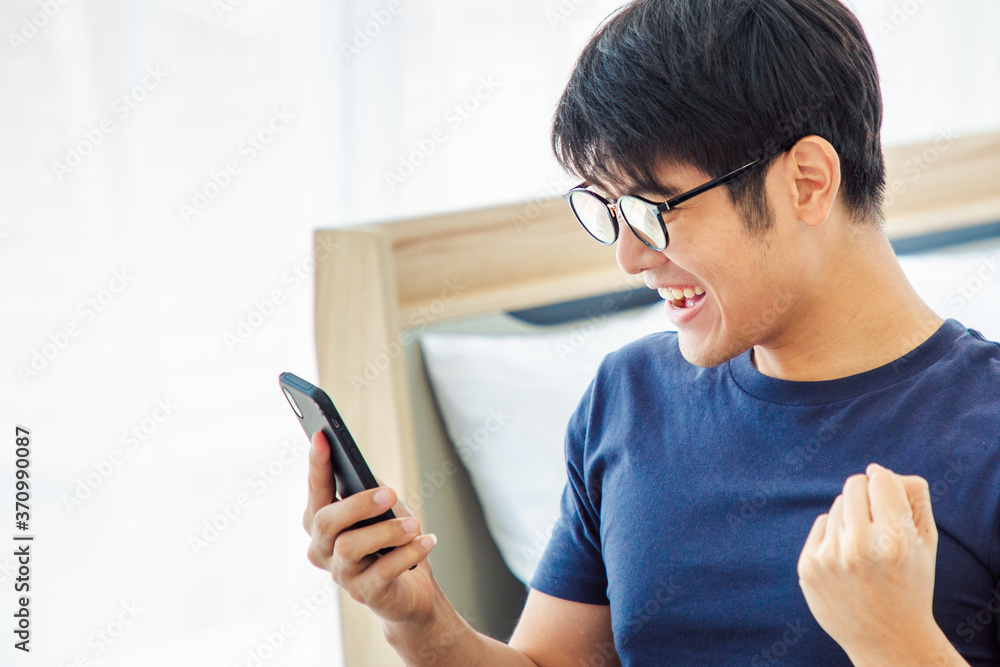 Surprised happy asian man using mobile phone on desk read good news on internet, amazed asian guy winner excited win scream with joy celebrate victory success at home. With Copy Space. Surprised happy asian man using mobile phone on desk read good news on internet, amazed asian guy winner excited win scream with joy celebrate victory success at home. With Copy Space.