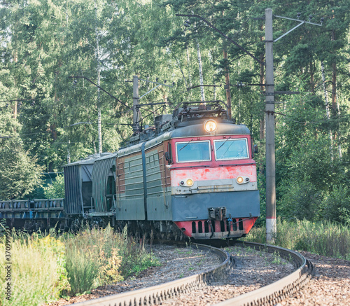 Freight train moves by the forest at summer day time.