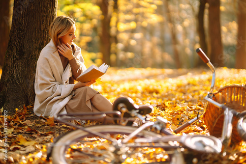 Stylish woman reading a book in the autumn park. Relaxation  enjoying  solitude with nature.
