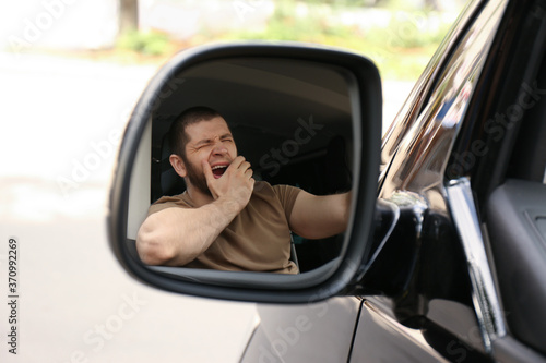 Slika na platnu Tired man yawning in his auto, view through car side mirror