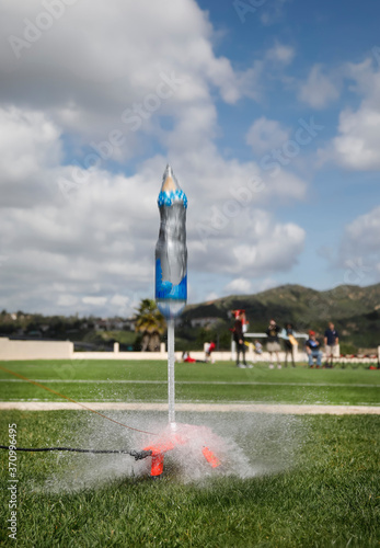 Water bottle rocket launch with rocket blurred from speed. Children out of focus in background on blue sky cloud backgound