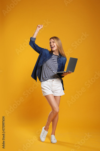 Full length portrait of emotional woman with modern laptop on yellow background