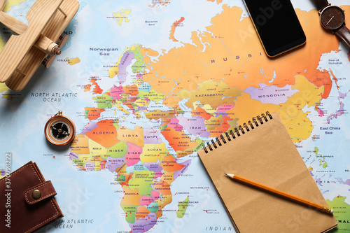Flat lay composition with notebook and different items on world map. Trip planning