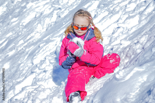 Young Girl Sitting On The Snow Mountain and playing with snow ball. Winter time
