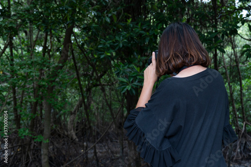 A woman in a black shirt stands back to take pictures in the dark forest.