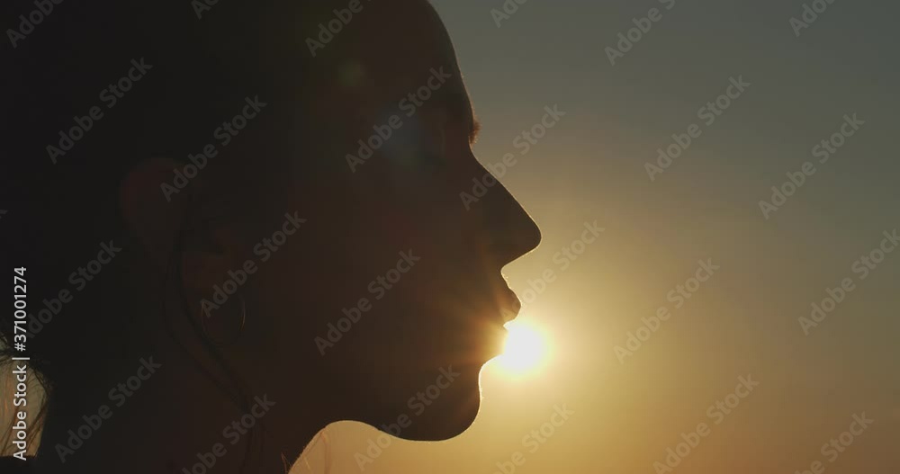 Close up female face profile silhouetted on evening sky setting sun slow motion. Happy woman kissing sun on nature background outdoors copy space text. Summer skin care products concept Close up female face profile silhouetted on evening sky setting sun slow motion. Happy woman kissing sun on nature background outdoors copy space text. Summer skin care products concept