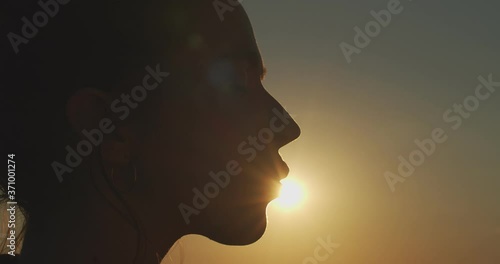 Close up female face profile silhouetted on evening sky setting sun slow motion. Happy woman kissing sun on nature background outdoors copy space text. Summer skin care products concept