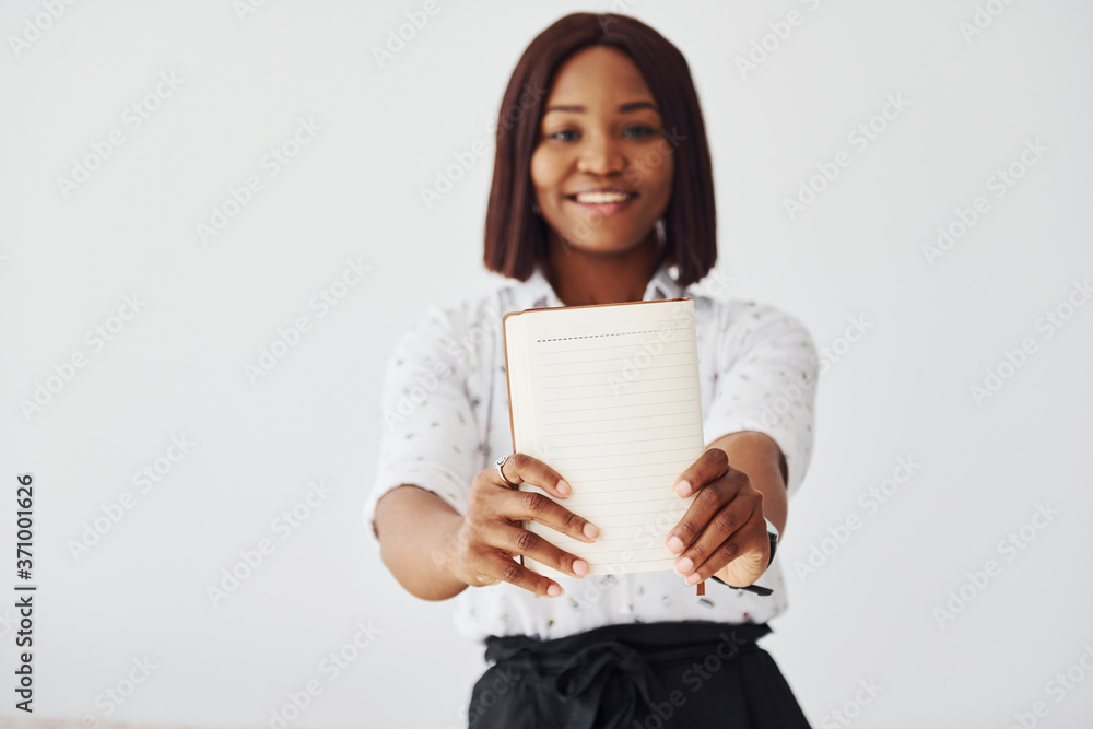 Young african american woman in formal clothes standing with notepad and empty paper in hands indoors Young african american woman in formal clothes standing with notepad and empty paper in hands indoors