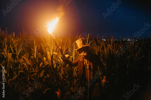 Photographie Walking dead zombie stands in cornfield with burning torch.