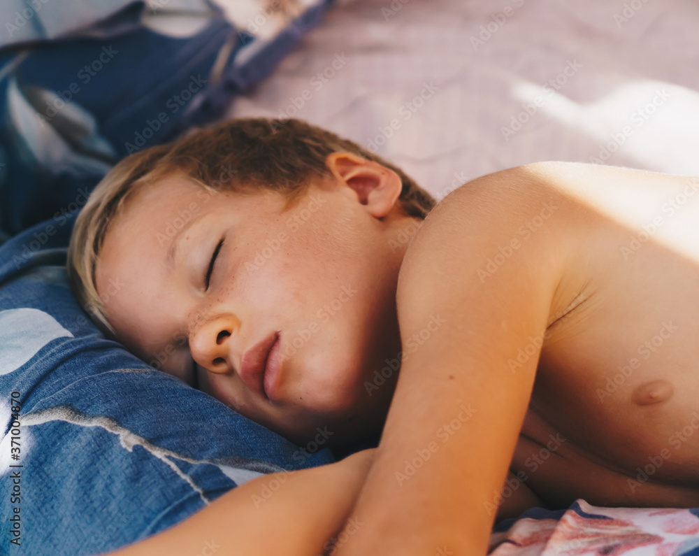 Cute little boy sleep sweetly on pillow with bright morning sunbeams from window, taking a nap. Happy bedtime for kids. Problem of early awakening, late falling asleep, health sleep biorhythms Cute little boy sleep sweetly on pillow with bright morning sunbeams from window, taking a nap. Happy bedtime for kids. Problem of early awakening, late falling asleep, health sleep biorhythms