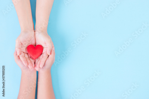 Woman and child holding heart on light blue background. Concept for charity, health insurance, love, international cardiology day. World Heart Day or Donation concept.