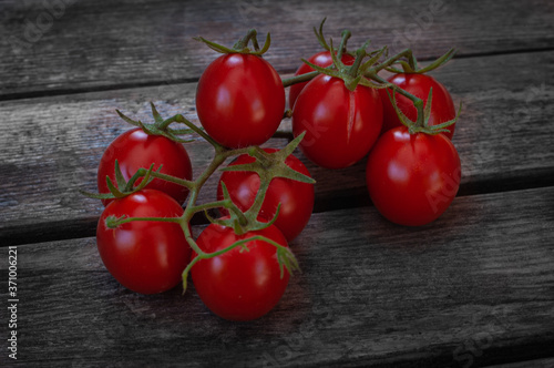 Fresh red cherry tomatoes on a brunch lying on a wooden old background. Closeup photo of organic vegetables and healthy food