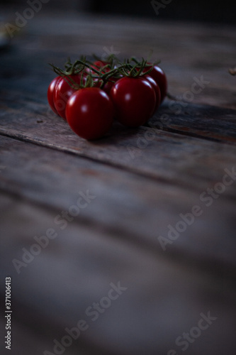 Several juicy bright red cherry tomatoes lying on top of a vertical photo on a blurred background of an old wooden table. Close up photo of healthy fresh vegetables