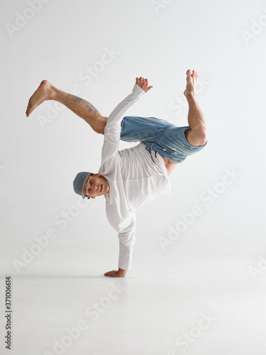 Fototapeta Naklejka Na Ścianę i Meble -  Young breakdancer stands on one arm dancing hip-hop isolated on white background. Break dance school poster