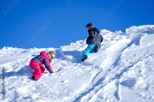 Two joyful kids playing on the snowing mountain on a winter day.