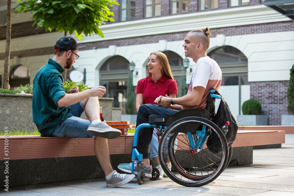 © master1305 - Group of friends taking a stroll on city's street in summer day. Disabled, handicapped man with his friends having fun. Inclusion and diversity concept, normal lifestyle of special groups of society.
