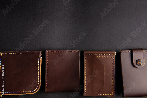 beautiful background wallets made of genuine leather of brown color made by hands are laid out on a black table. view from above. With space for an inscription. Leather craft concept.