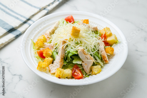 Salad caesar with chicken on white plate on marble table