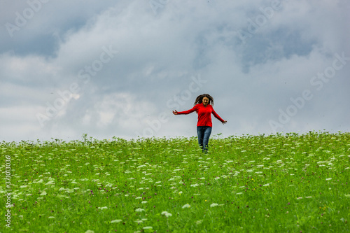 Frau mit rotem Sweatshirt springt in einer Grüner Wiese
