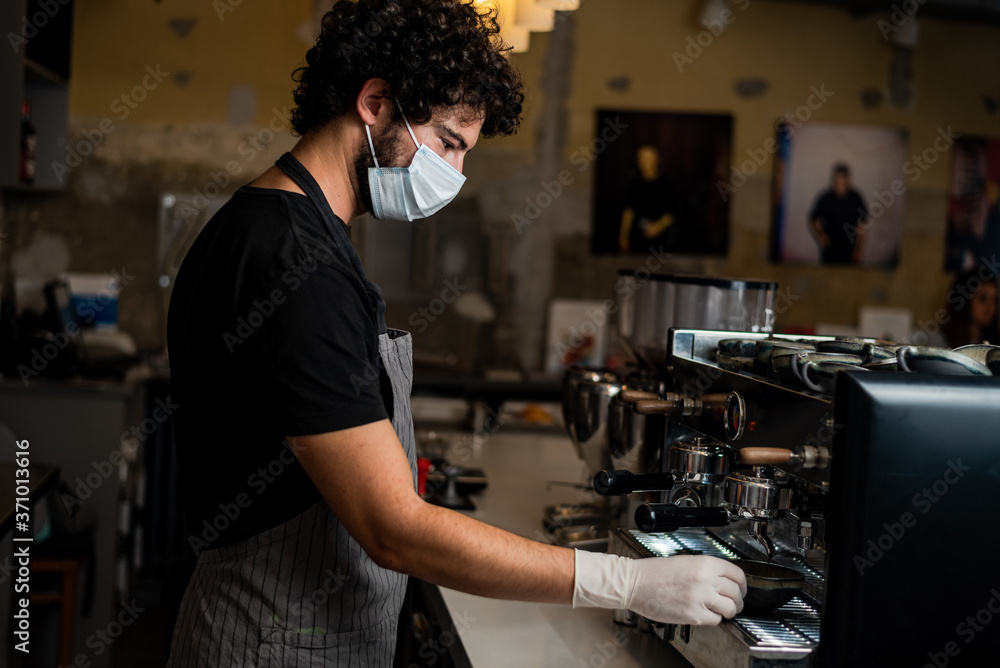 Young man, barista, making coffee espresso while wearing surgical mask and gloves for preventing corona virus spread - Bar safety working concept. Young man, barista, making coffee espresso while wearing surgical mask and gloves for preventing corona virus spread - Bar safety working concept.