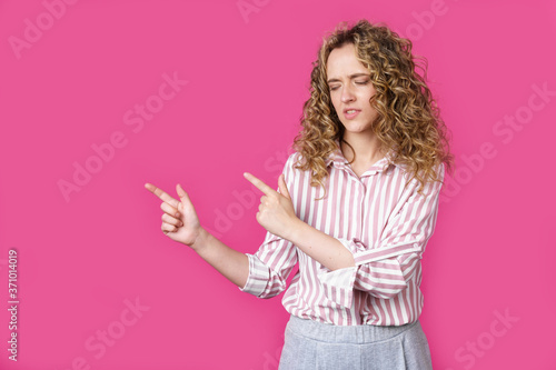 A woman points to a copy space, discusses an amazing advertisement, gives way or a direction, wears a striped shirt