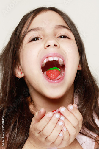 Photos retrato de muy cerca de niña mostrardo una gominola de fresa que tiene en la boc