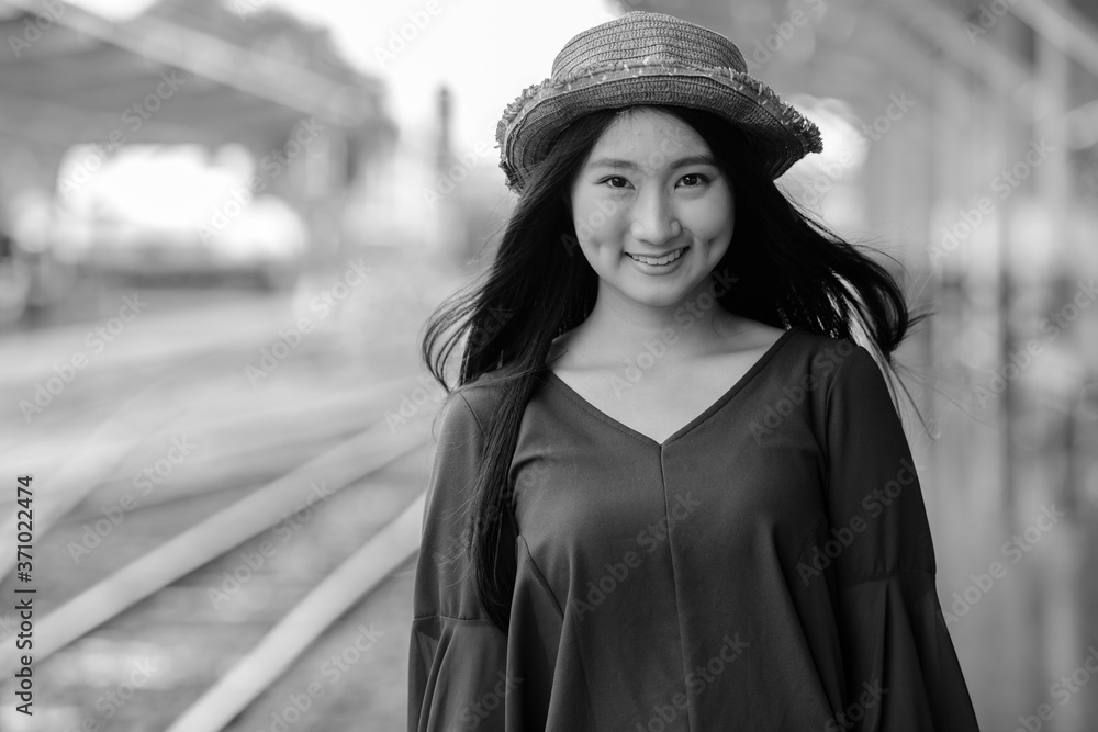 Happy young beautiful Asian tourist woman at the railway station in black and white