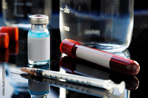 Vaccine bottle with a blue liquid, a syringe and a blood sample on a laboratory like background