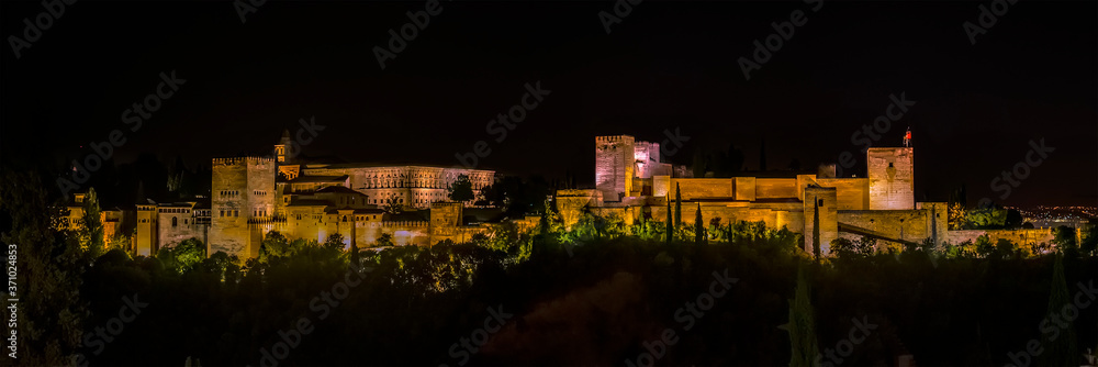 A panorama view from Saint Nicholas Square, Granada, Spain towards the Alhambra district at night in the summertime