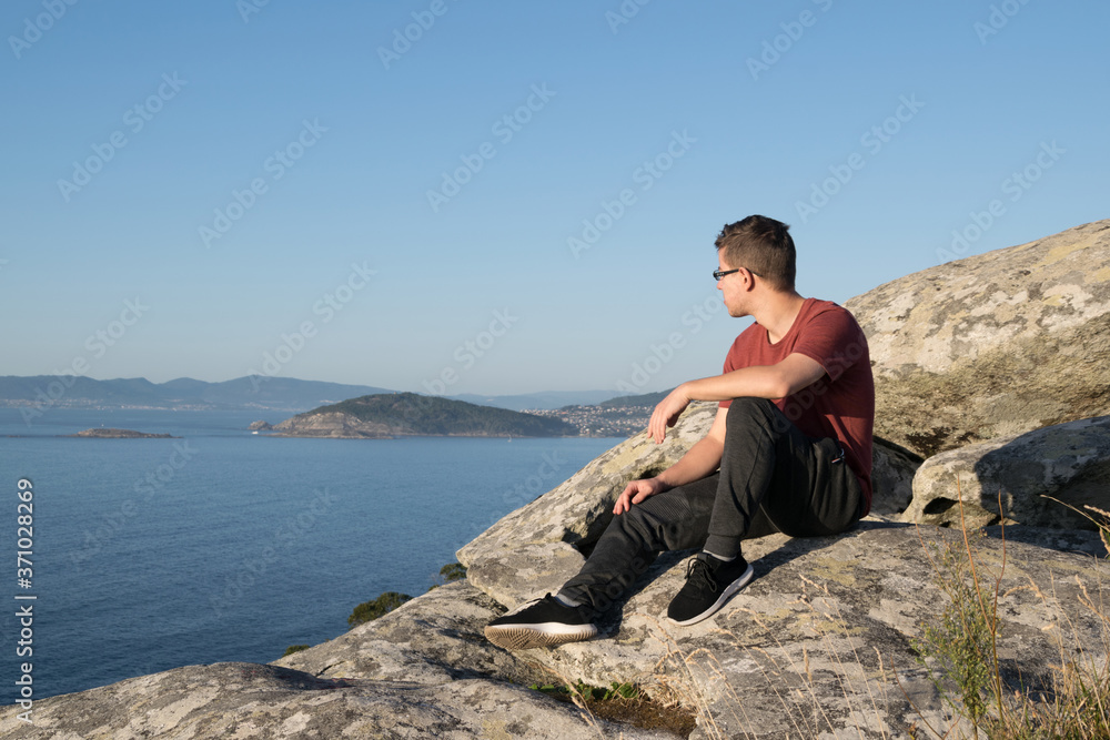 Boy sitting on the rocks of a mountain looking at the ocean