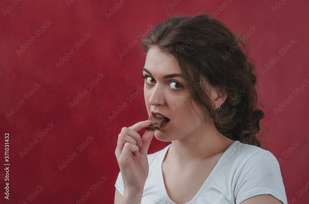 Pretty girl eating chocolate. Portrait on red background, delicious food, sweet chocolate Pretty girl eating chocolate. Portrait on red background, delicious food, sweet chocolate
