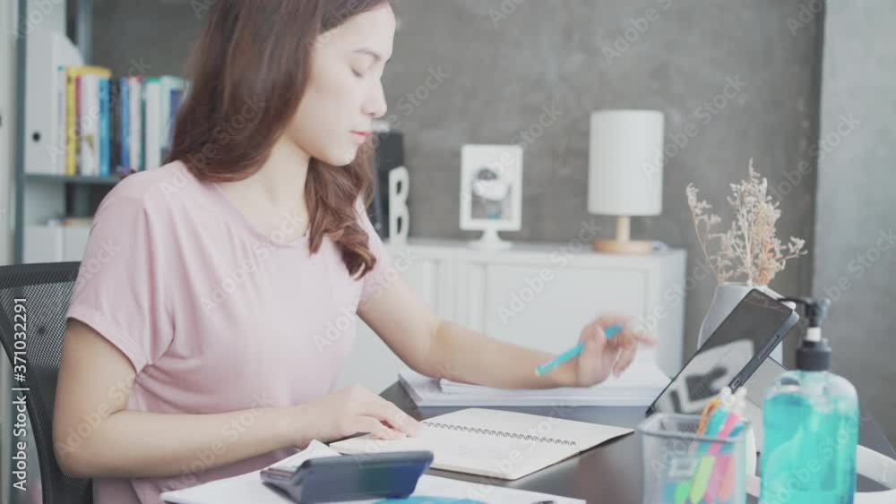 Side view of Young beautiful Asian businesswoman use tablet and taking notes. Freelance woman work and quarantine at home office while corona virus prevention. New normal, lock down concept. Side view of Young beautiful Asian businesswoman use tablet and taking notes. Freelance woman work and quarantine at home office while corona virus prevention. New normal, lock down concept.