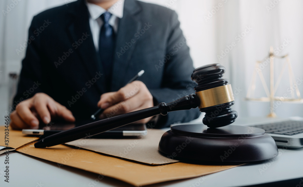 Justice and law concept.Male judge in a courtroom with the gavel, working with, computer and docking keyboard, eyeglasses, on table in morning light Justice and law concept.Male judge in a courtroom with the gavel, working with, computer and docking keyboard, eyeglasses, on table in morning light