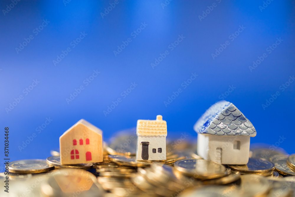 Business, Mortgage, Home Loan Concept. Closeup of three mini house toy on top of pile of gold coins on blue background with copy space.