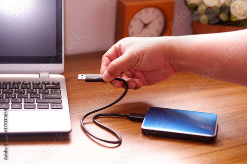 Man's hand was connecting an external portable hard disk usb 3.0 cable to laptop computer on desk, Data transfer or backup personal files concept